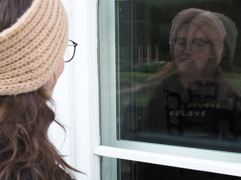 Beloved Gründerin Annabel sieht sich in der Reflektion einer Fensterscheibe. Ein Symbolbild für positive Affirmationen, Selbstliebe und Selbstannahme..