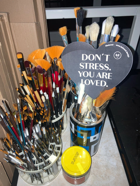 Ein BELOVED-Sticker mit den Worten "Don't Stress. You are loved." Steckt in einem Becher voller Pinseln. Ein Symbolbild für positive Affirmationen und Achtsamkeit..